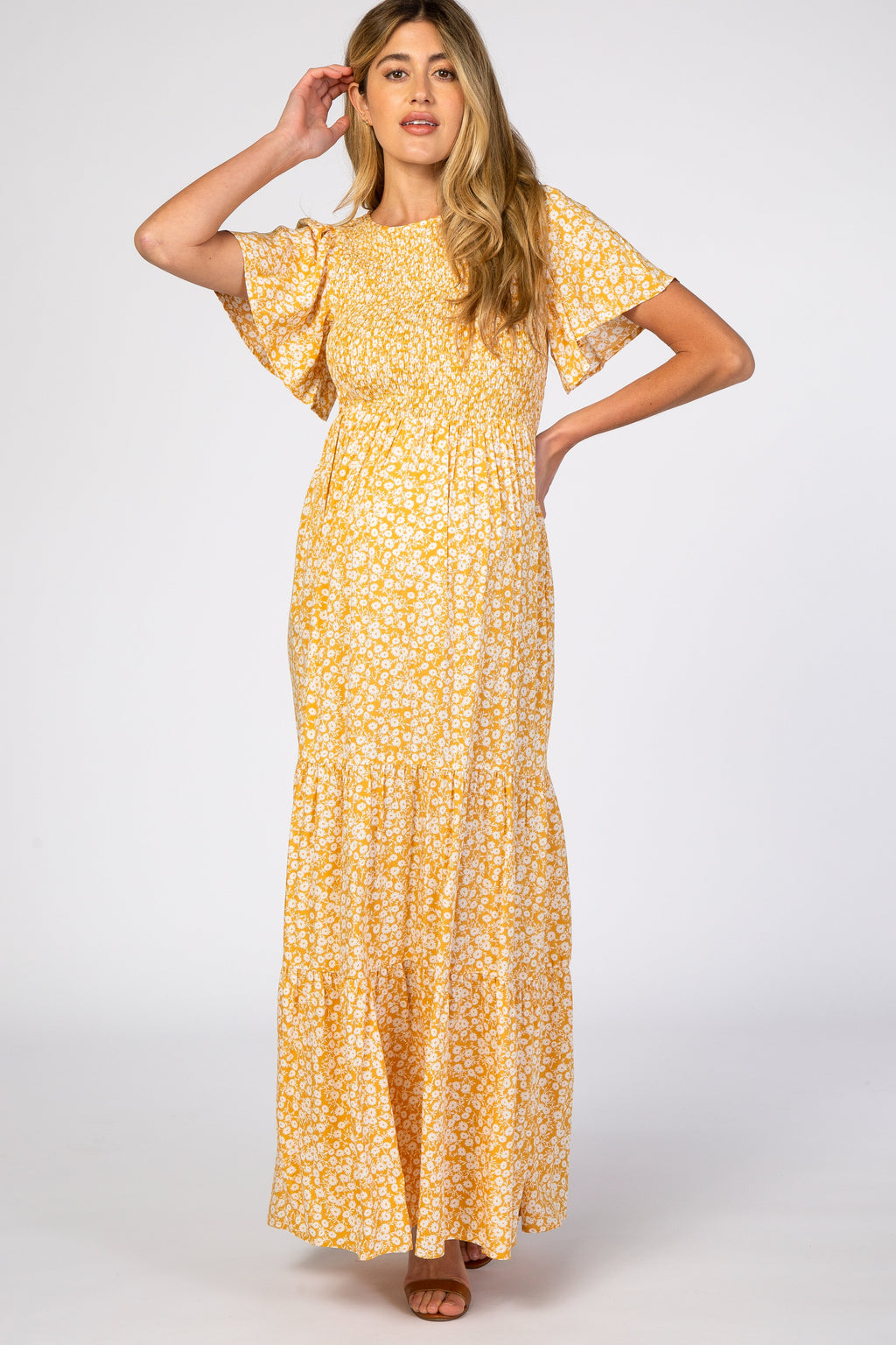 A pregnant woman wearing a yellow floral print maternity maxi dress with a smocked bodice and flutter sleeves, standing against a neutral background.