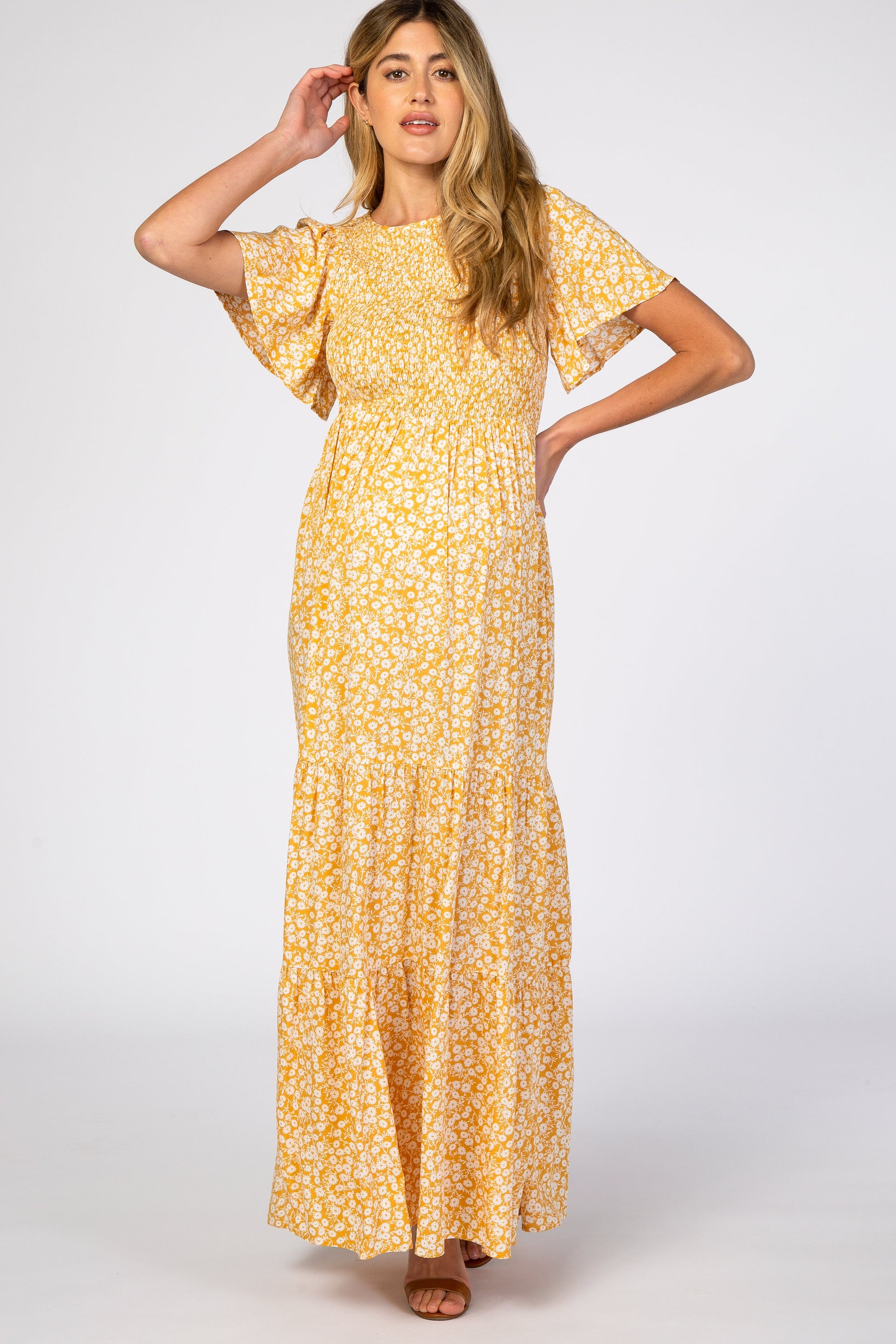 A pregnant woman wearing a yellow floral print maternity maxi dress with a smocked bodice and flutter sleeves, standing against a neutral background.