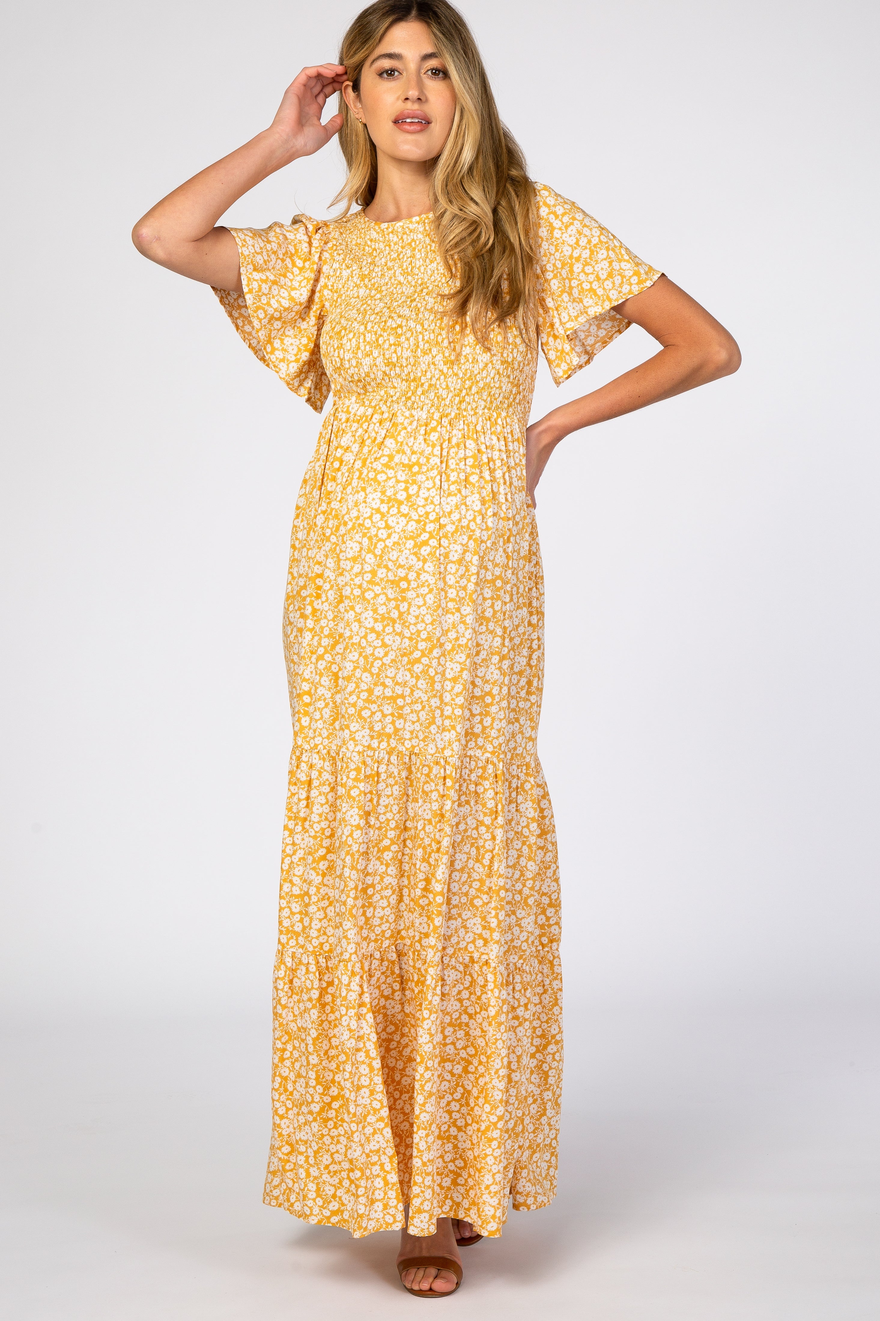A pregnant woman wearing a yellow floral print maternity maxi dress with a smocked bodice and flutter sleeves, standing against a neutral background.