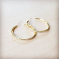 A pair of gold-tone hoop earrings with delicate pave-style crystal inlay resting on a light wooden surface.