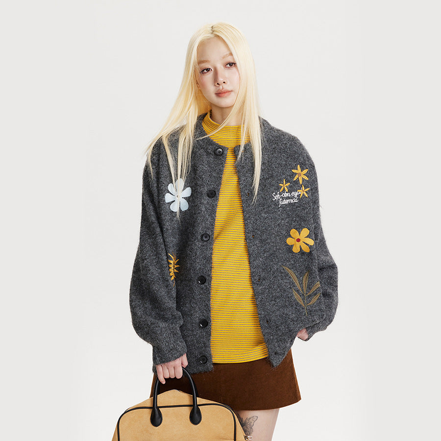 A woman wearing a charcoal grey button-up cardigan with yellow and white floral embroidery designs.