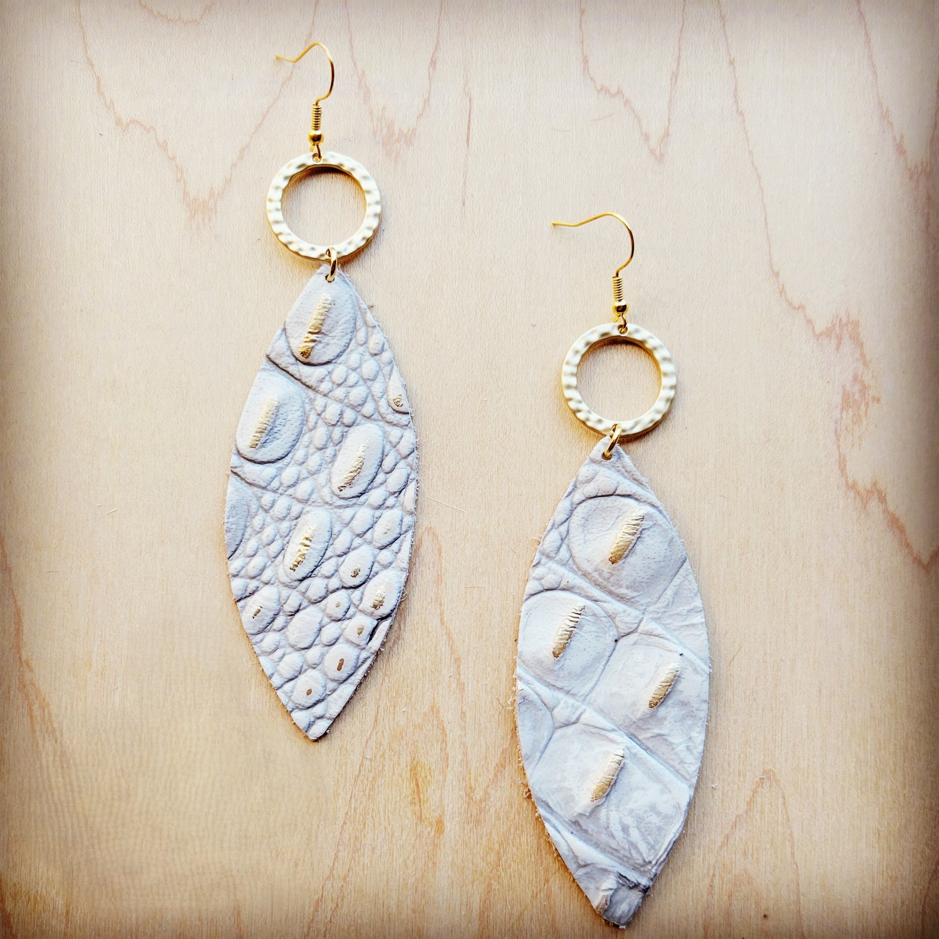 White and gold gator-embossed oval leather earrings hanging from hammered matte gold-tone hoops.