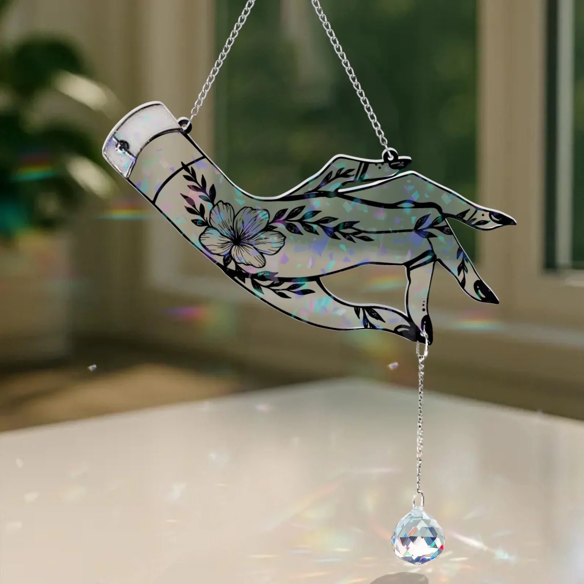 A holographic acrylic witchy hand window hanging with mystical tattoo designs and a crystal prism charm hanging from a chain.