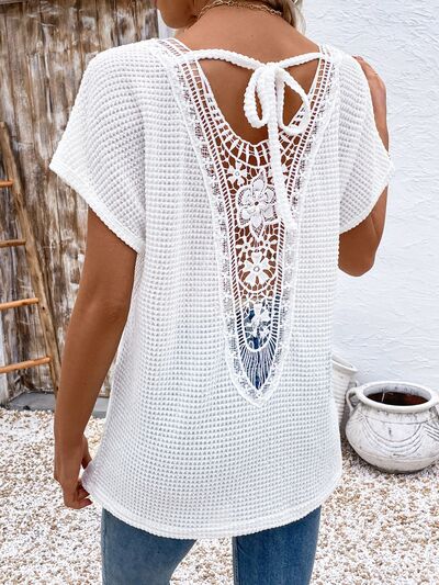 Back view of a woman wearing a white waffle knit short sleeve t-shirt with a detailed lace back panel and tie closure.