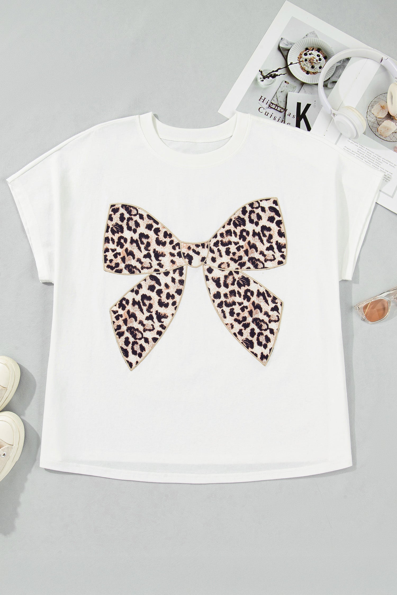 A white short-sleeved t-shirt with a large leopard print bow embroidery patch on the front, displayed flat on a neutral background.