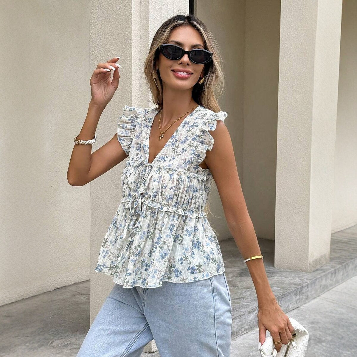 A woman wearing a blue floral chiffon sleeveless top with flutter sleeves and a matching blue floral A-line skirt.