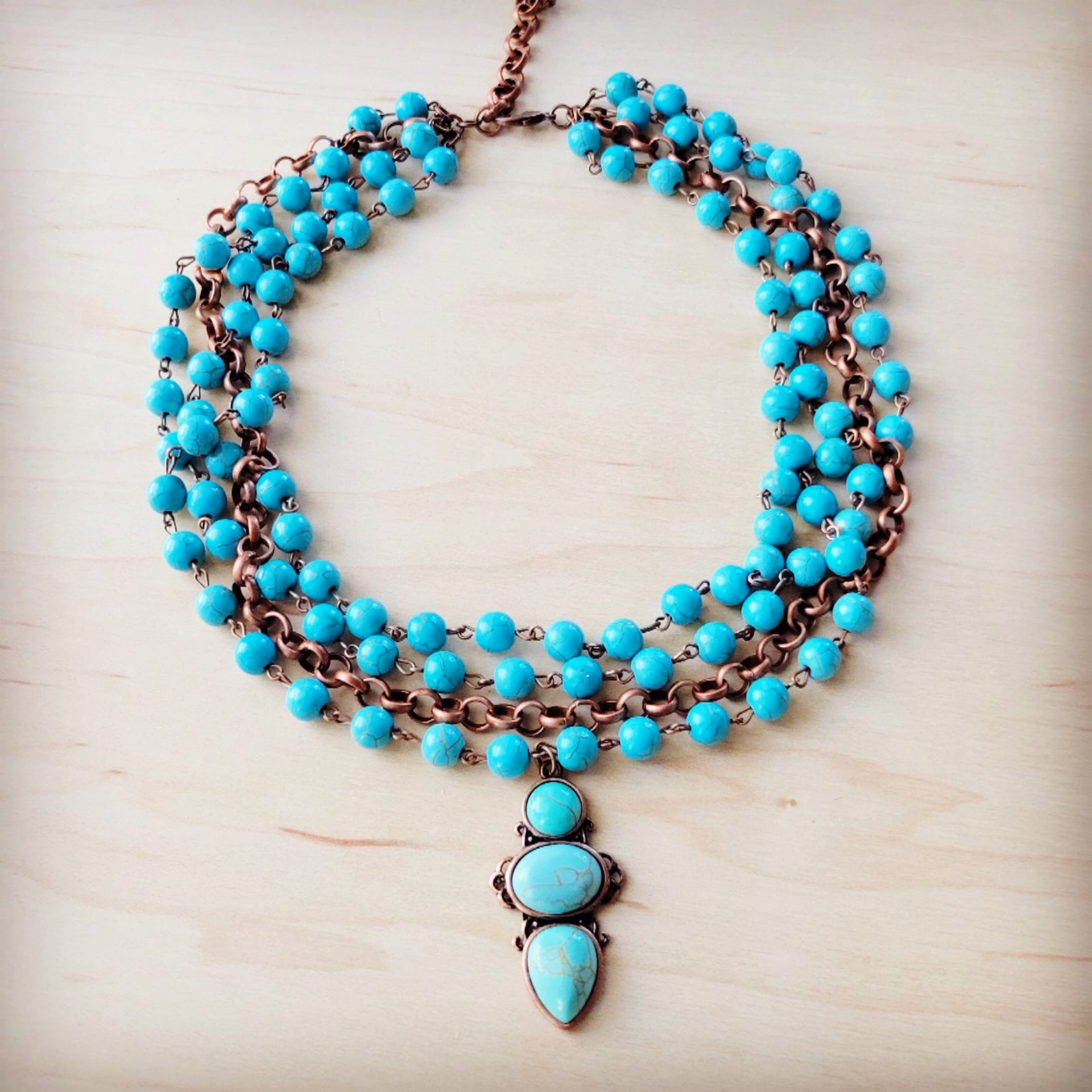 Triple strand turquoise bead necklace with a copper-tone chain and three-stone droplet pendant.