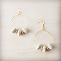 A pair of gold-tone hoop earrings featuring white ridged shell beads and small gold spacers on a light wood background.