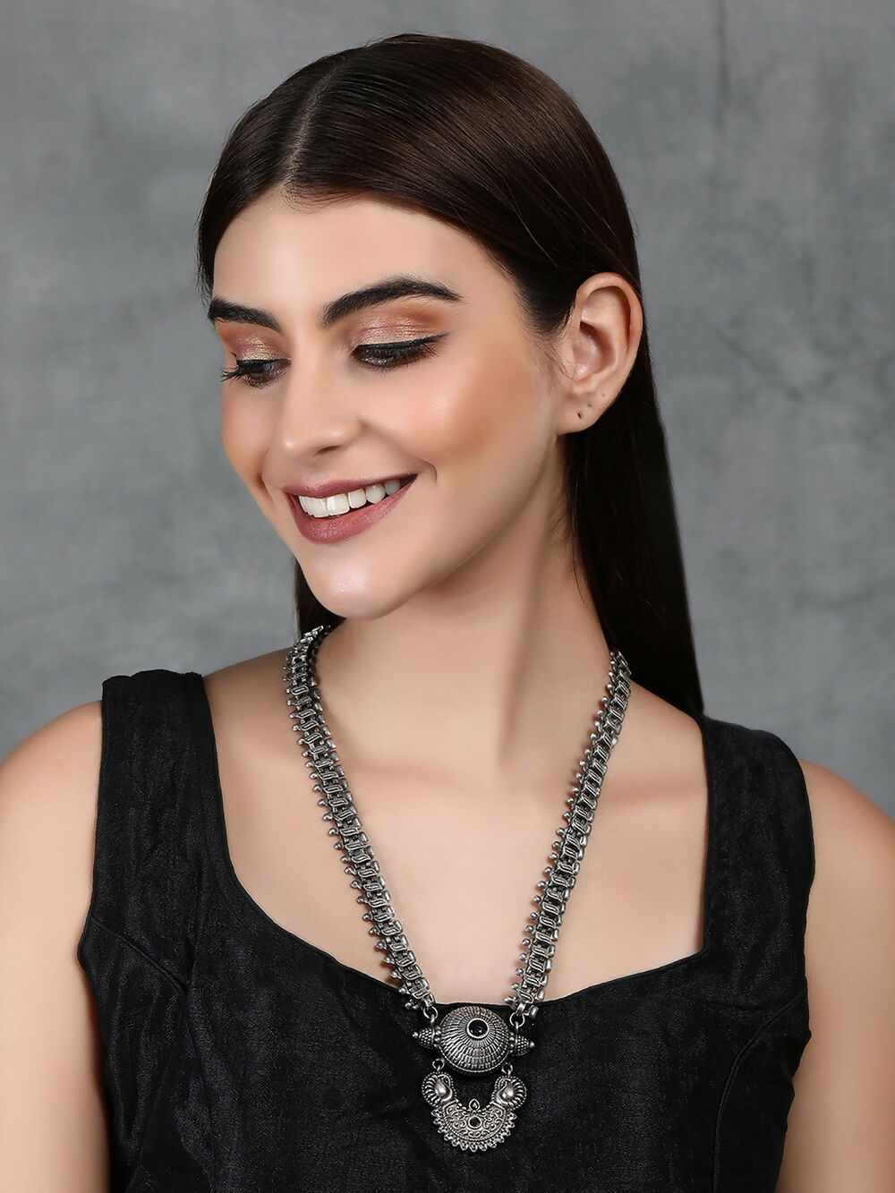 Close up of long silver-tone brass statement necklace with intricate patterns and stones
