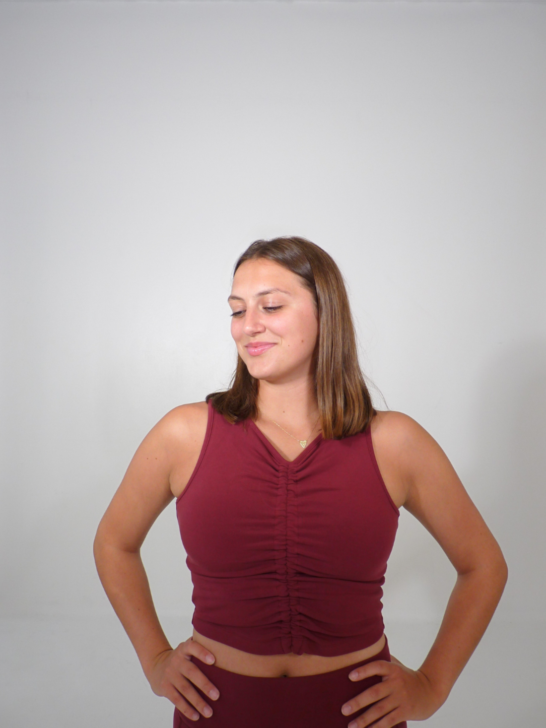 A woman wearing a maroon ruched front tank top with matching leggings standing against a neutral background.