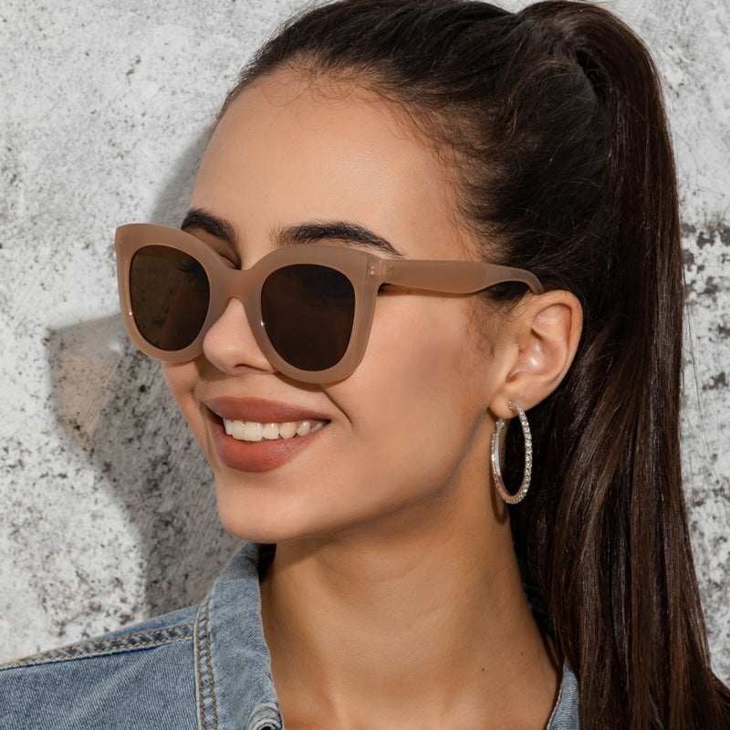 A pair of oversized beige large rim sunglasses for women against a minimalist background.
