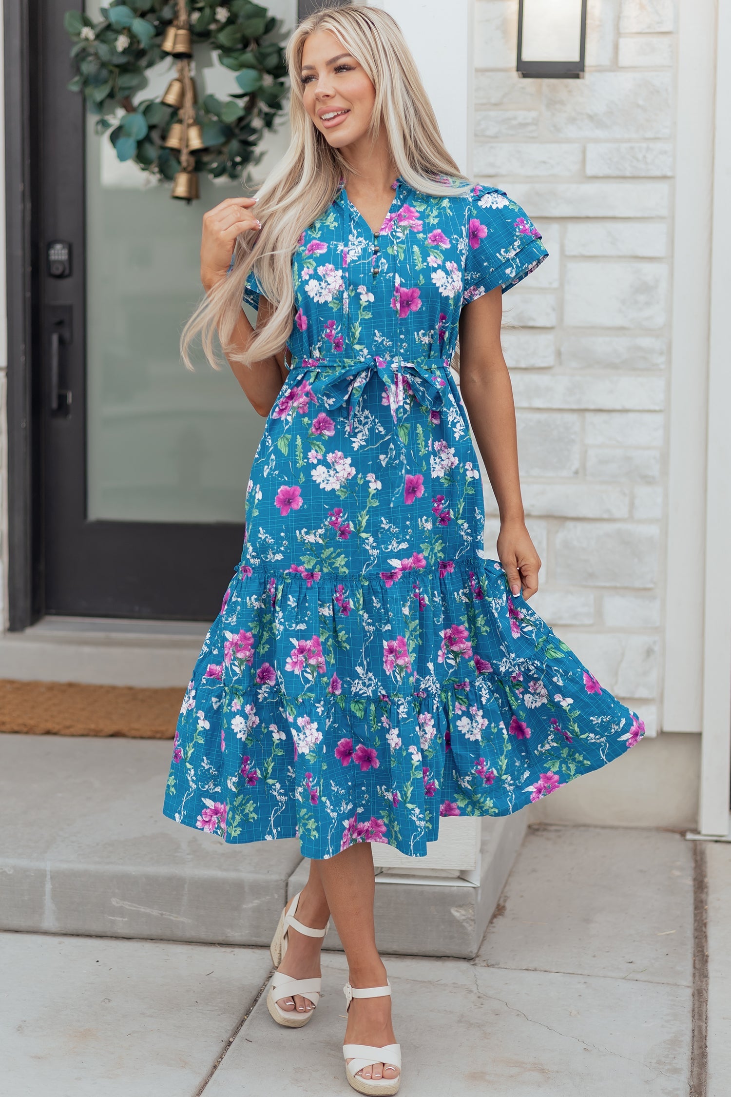 Model wearing a blue floral long dress with flutter sleeves, split neck, and a tie-belt waist.