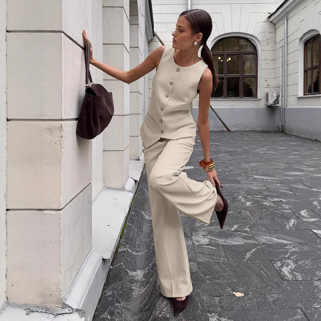 A woman wearing a beige button-front sleeveless vest and matching wide-leg pants standing in an urban setting.