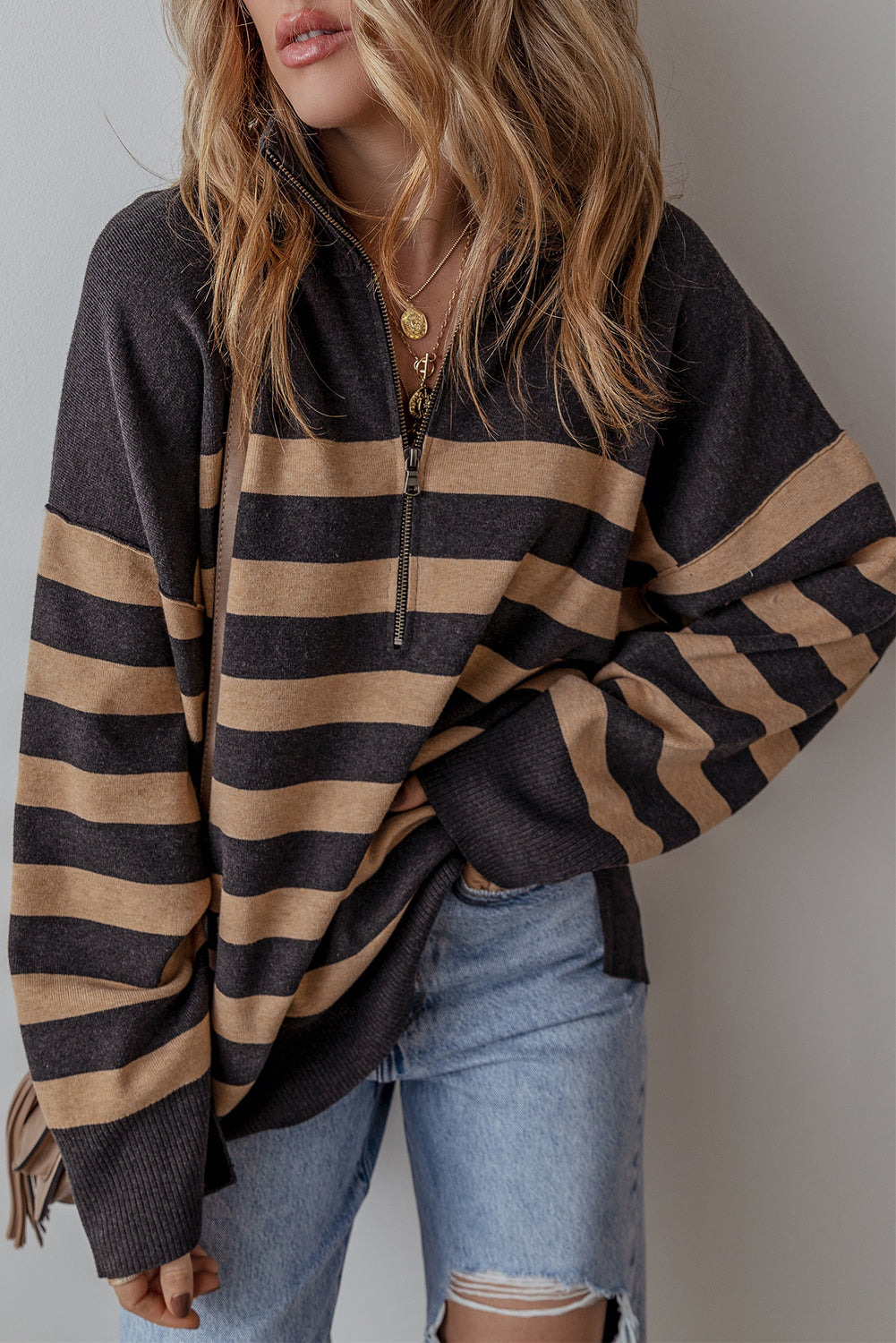 Person wearing a black and brown striped sweater with light blue jeans against a neutral background