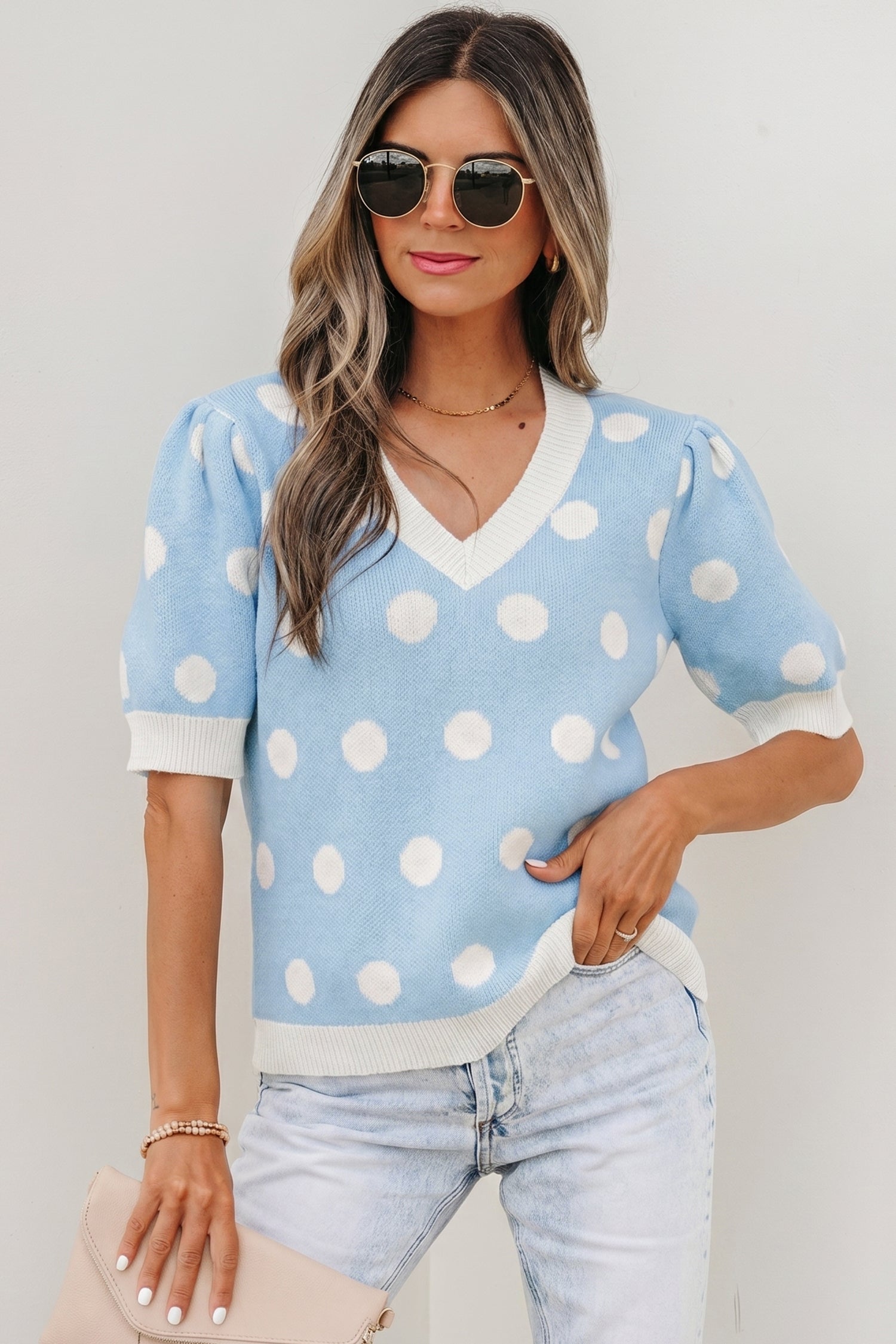 Woman wearing a white and light-blue polka dot short sleeve sweater with puff sleeves and V-neckline.