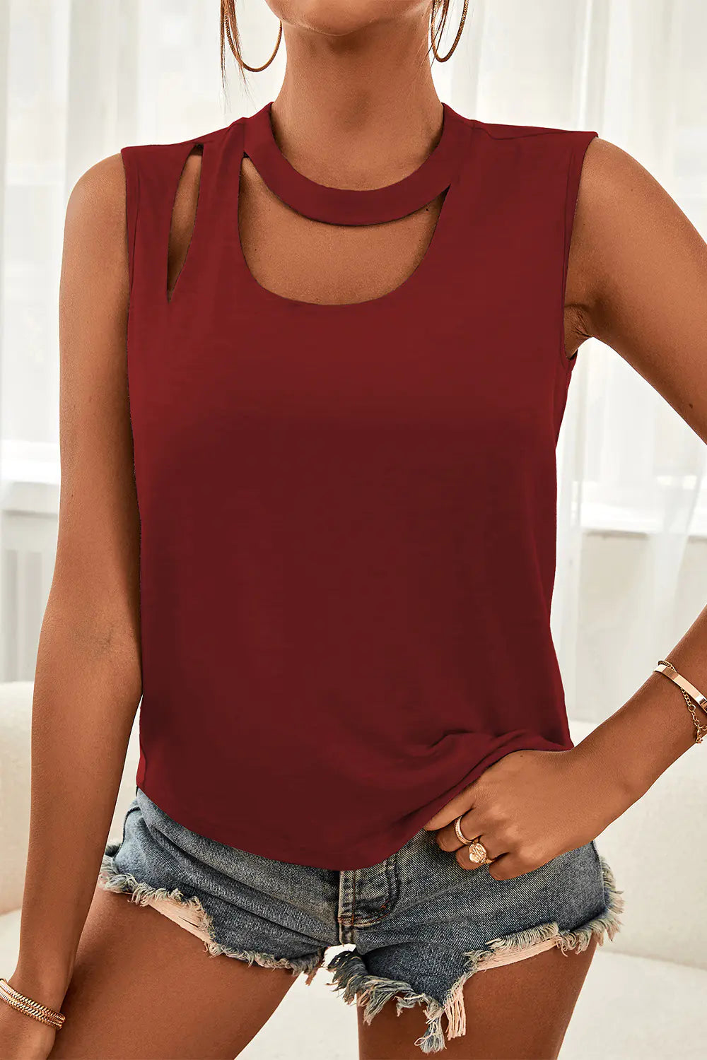 A woman wearing a solid color sleeveless tank top with a stylish shoulder cutout detail, styled with denim shorts.
