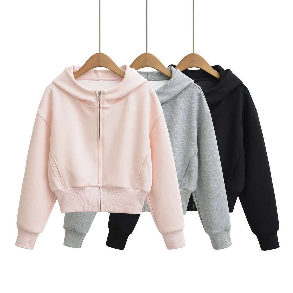 Three women's cropped full-zip hoodies in pink, grey, and black, hanging on wooden hangers against a white background.