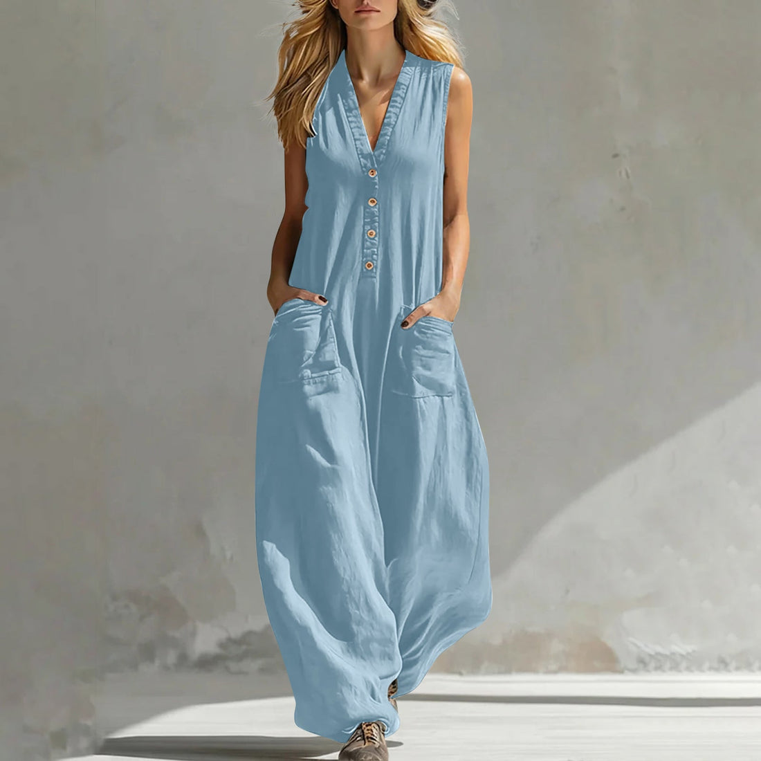 A woman wearing a light blue sleeveless wide-leg jumpsuit with button details and pockets.