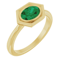 Close-up of a 14K yellow gold ring with an oval emerald set in a geometric hexagonal frame.