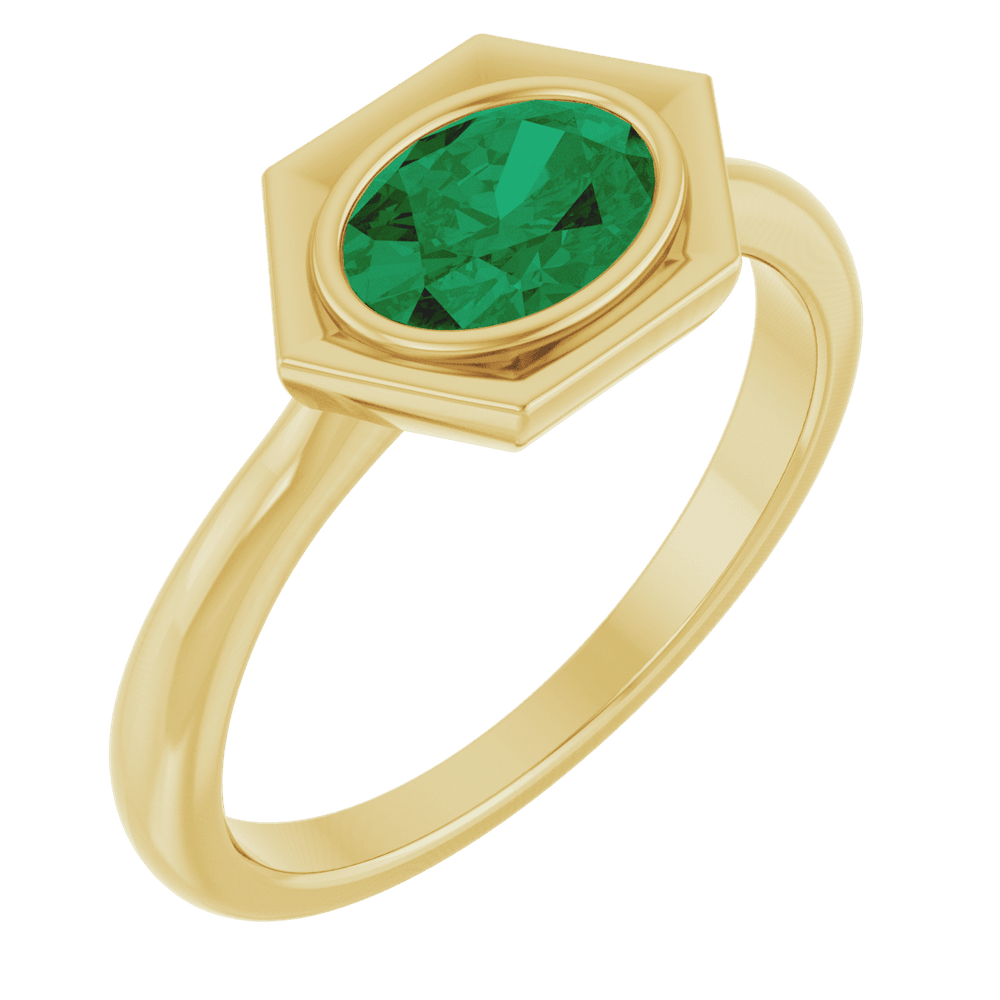 Close-up of a 14K yellow gold ring with an oval emerald set in a geometric hexagonal frame.