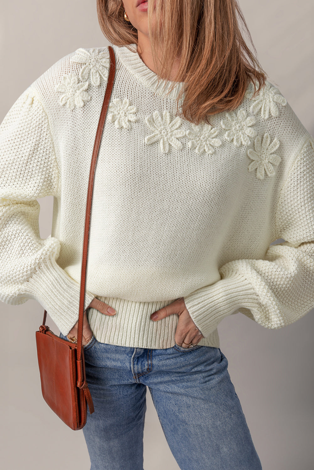 Close up of a woman wearing a white textured puff sleeve sweater with floral applique details on the chest.