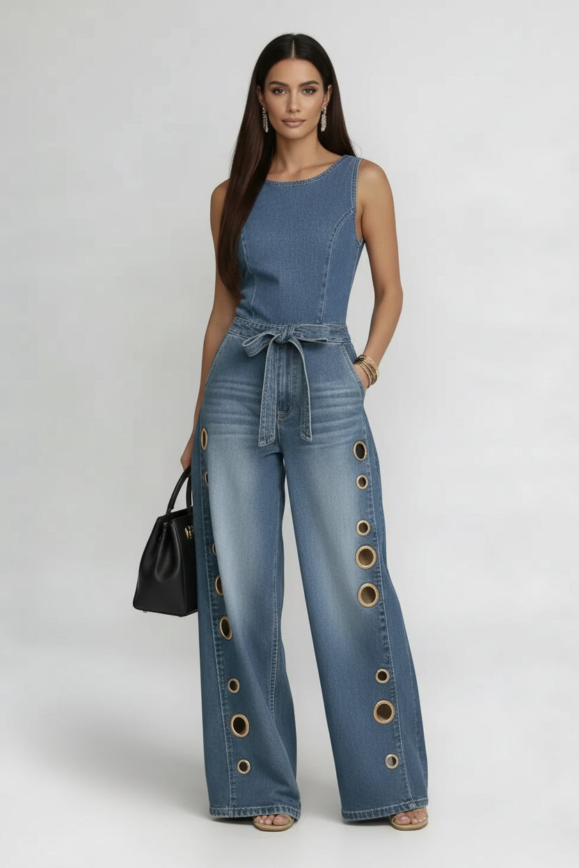 A woman wearing a sleeveless blue denim jumpsuit with gold grommet details on the wide legs.