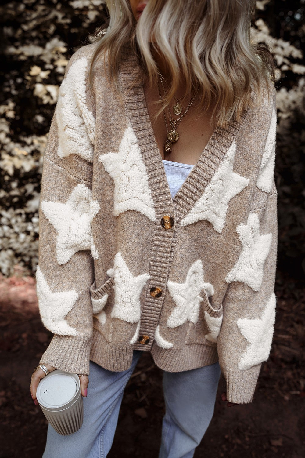 Close-up of a person wearing a beige and white star patterned button-up cardigan with pockets