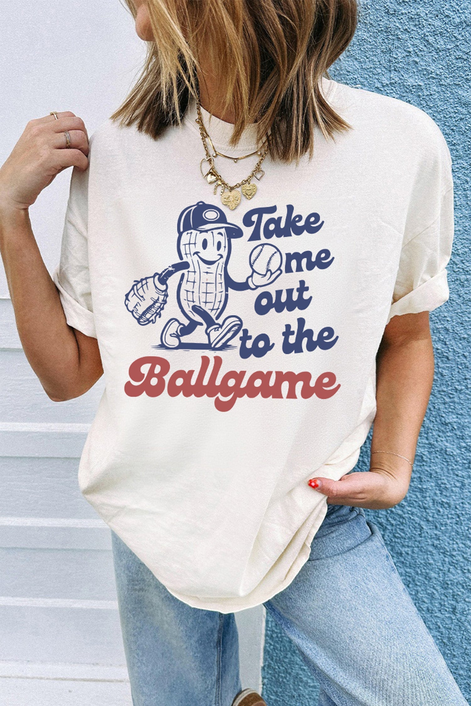 A woman wearing a white graphic t-shirt with Take Me Out To The Ballgame text and a peanut cartoon graphic.
