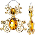 A pair of gold tone tunnel plug earrings featuring intricate scrolling metalwork and vibrant yellow oval gems, shown against a white background.