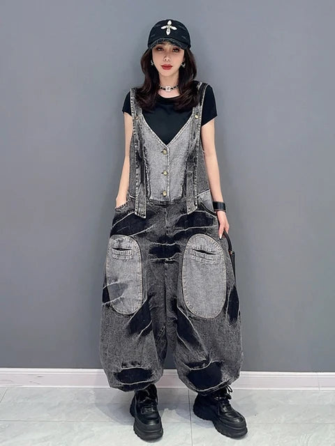 Woman wearing a washed black denim patchwork V-neck loose jumpsuit with large cargo pockets, styled with a black t-shirt and cap.