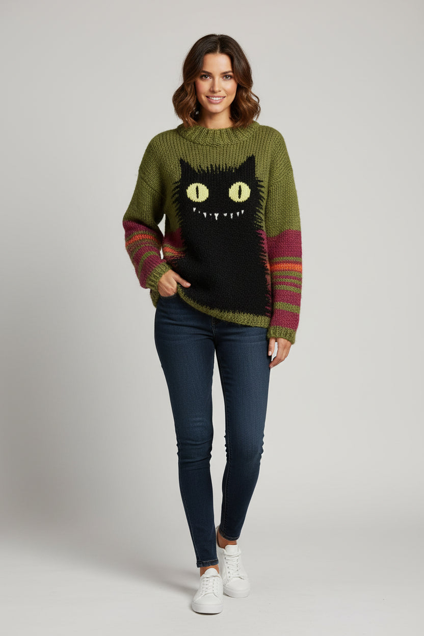 A retro-style, oversized green knit sweater with a prominent black cat graphic on the front, displayed against a wooden background.