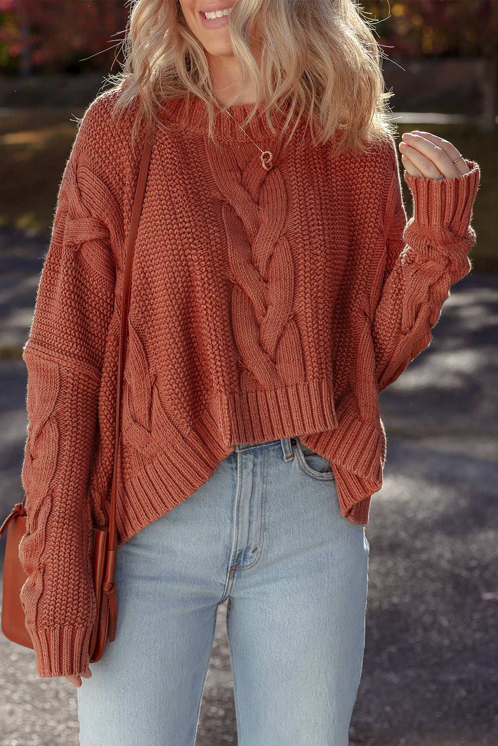 Close-up of a person wearing a burnt orange chunky cable knit sweater with a slouchy fit.