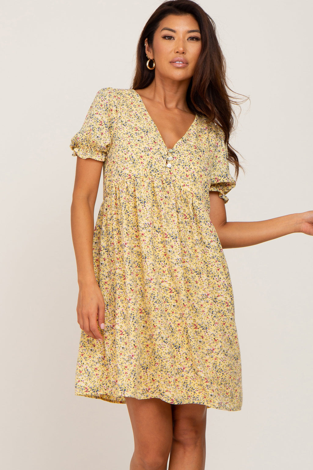 A woman wearing a bright yellow floral print mini dress with a v-neck and button front details.