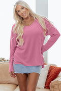 A woman wearing a pink ribbed v-neck long sleeve top with side slit design.