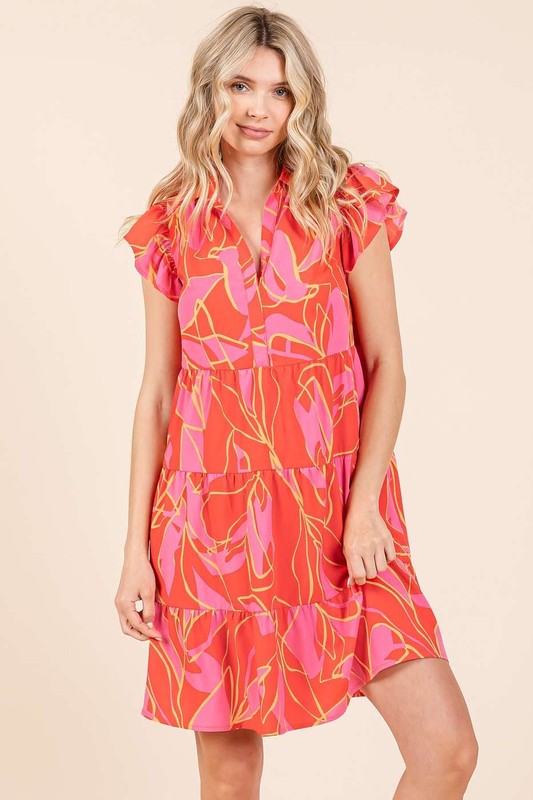 Woman wearing a vibrant leaf print tiered mini dress with ruffle sleeves in red, pink, and orange