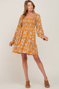 A woman wearing a yellow floral long-sleeve mini dress with a smocked bodice and square neckline.