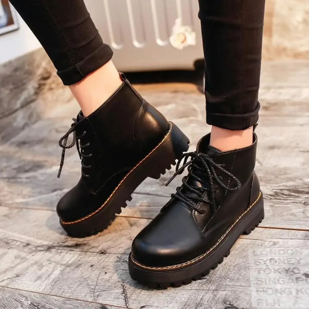 Close-up of a person wearing black Harajuku style retro platform lace-up ankle boots with a chunky sole on a light wooden floor.