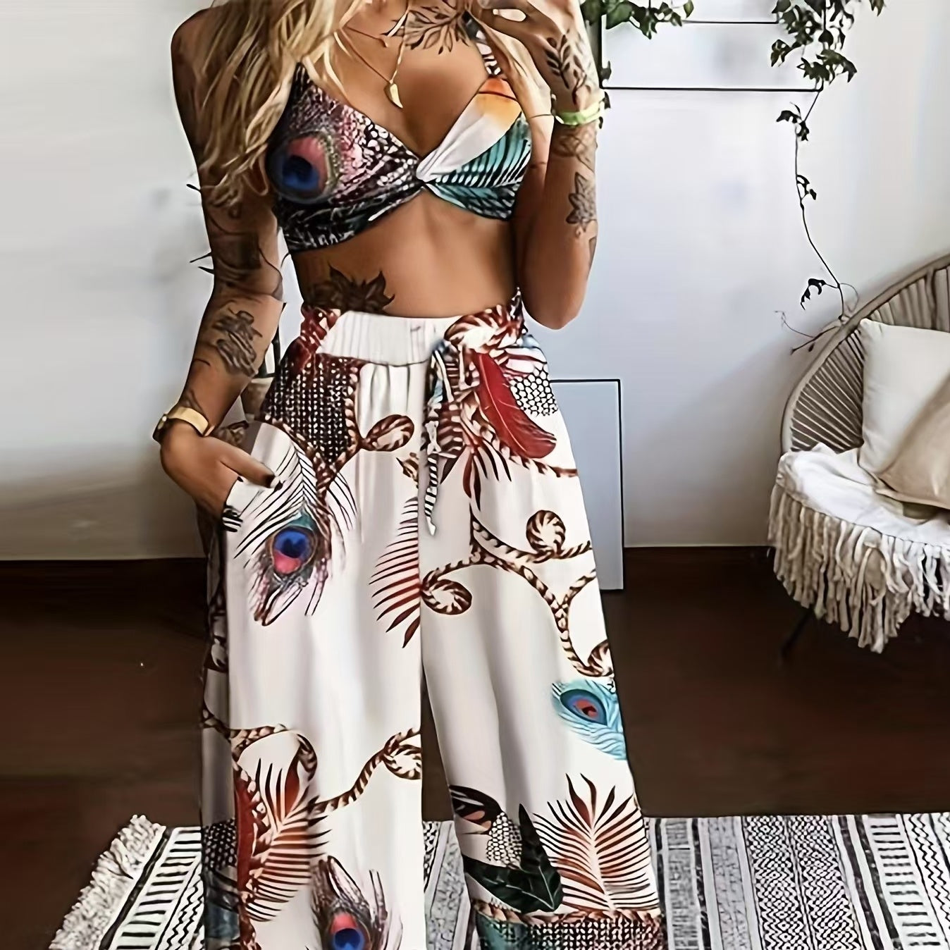 A woman wearing a two-piece white set with a colorful feather print, consisting of a twist-front crop top and wide-leg drawstring pants.