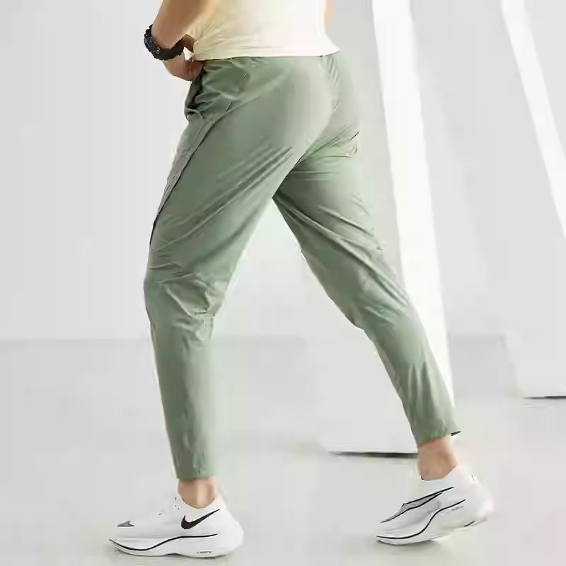 Side profile view of a woman wearing quick-dry elastic workout pants in olive green and black, styled with modern athletic sneakers.
