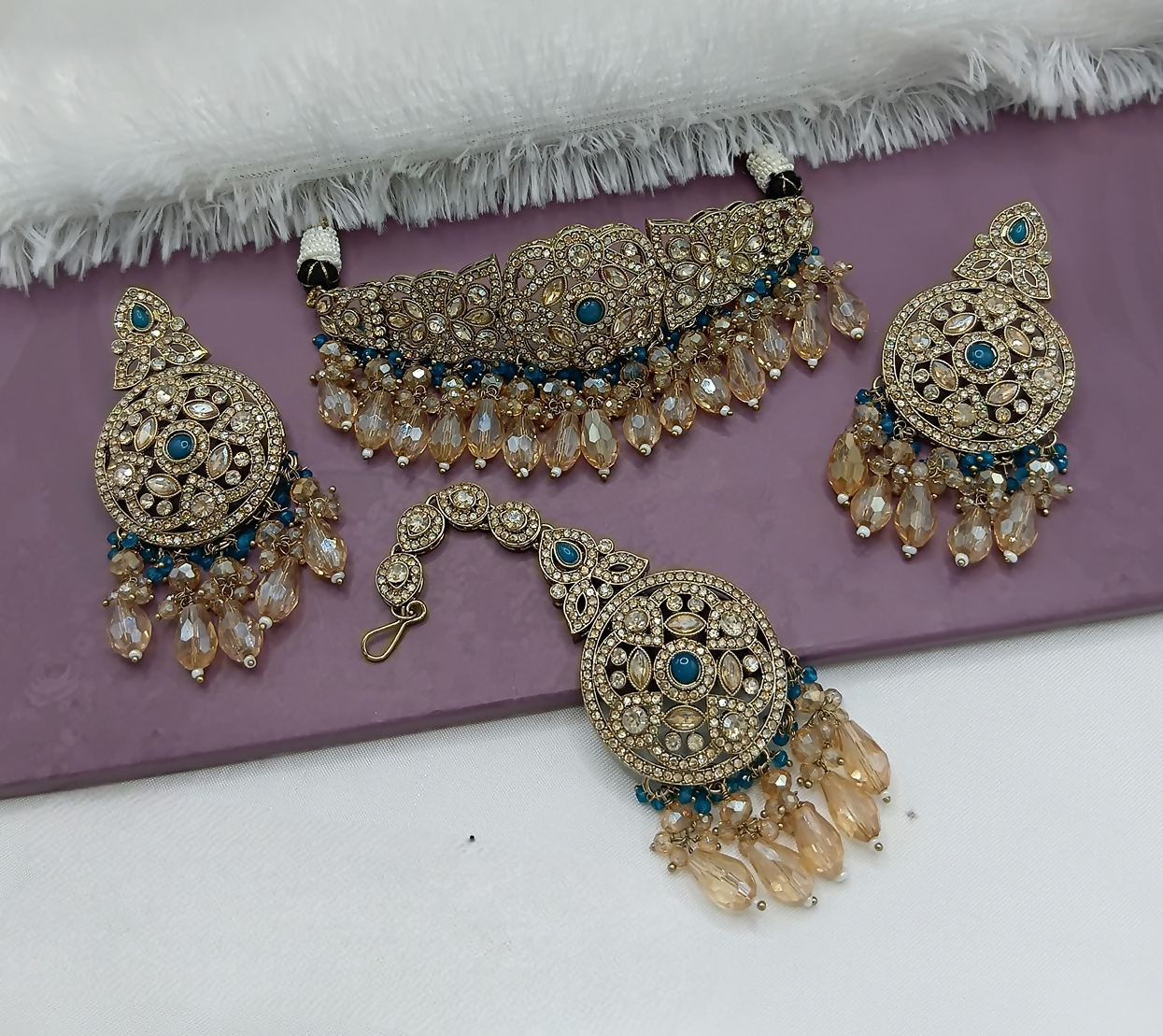 Close up of a vibrant teal blue alloy choker necklace set on a neutral background