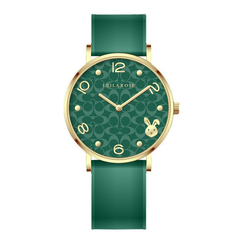 Close-up of a LEILAROSE Year of the Rabbit Limited Edition women's quartz watch with a green silicone strap and gold-tone casing. The watch face features a repeating monogram pattern, a rabbit icon at 3 o'clock, and gold numerals/markers. A second image shows the same watch with a red silicone strap.
