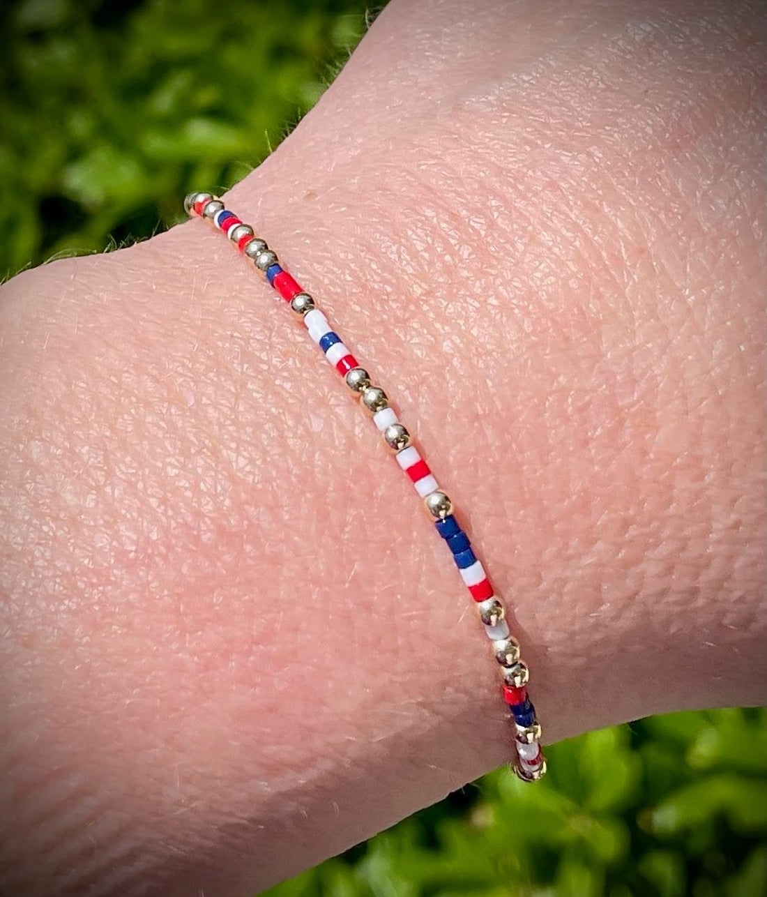Close up of a patriotic red, white, and blue seed bead and gold-filled bead bracelet on a wrist.