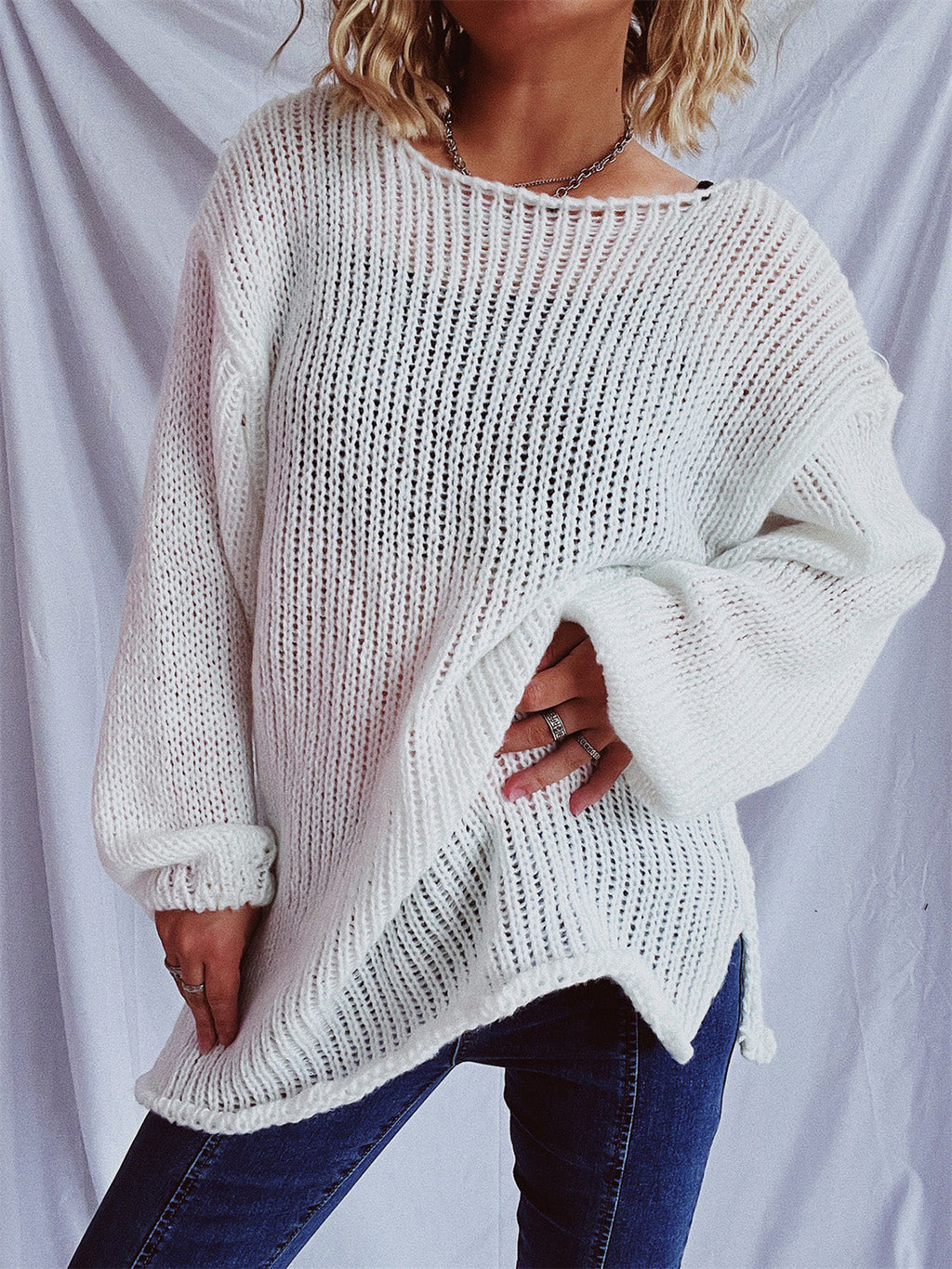 Woman wearing a white long sleeve boat neck dropped shoulder knit sweater with side slits