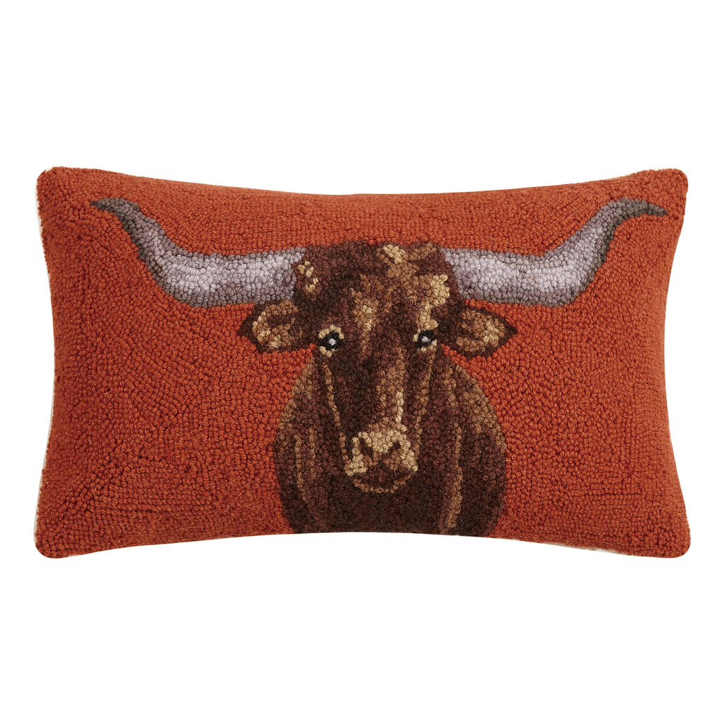 Rectangular 20x12 longhorn hooked wool lumbar pillow with rust background and velvet backing on a rustic living room sofa.