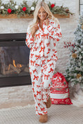 A woman wearing a white long-sleeve button-down pajama top and matching pants with a red bow print, standing in front of a fireplace and Christmas tree.