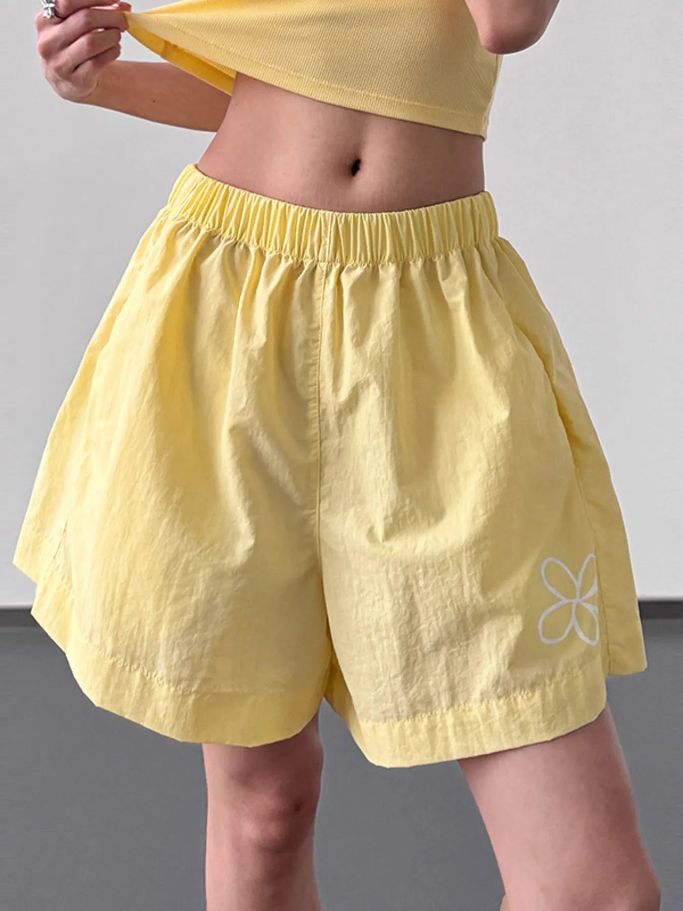 Model wearing bright yellow elastic waist shorts with a white flower graphic and side pockets