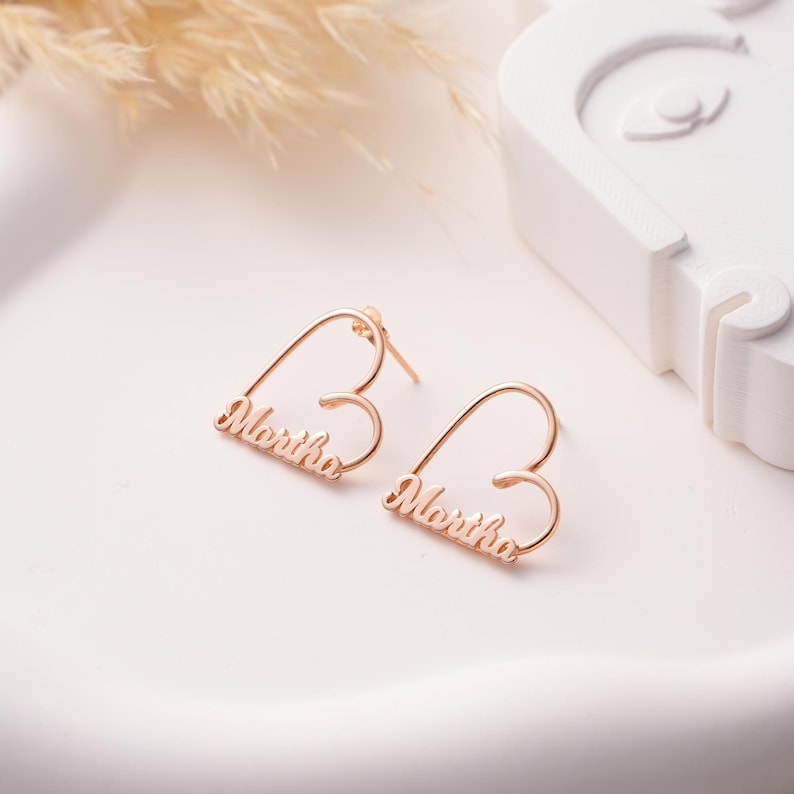 Custom-made heart-shaped stud earrings featuring a script name in a polished gold-tone finish.