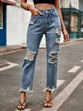 Model wearing blue denim jeans with heavy distressing on the knees and a raw frayed hem, styled with black strappy heels.