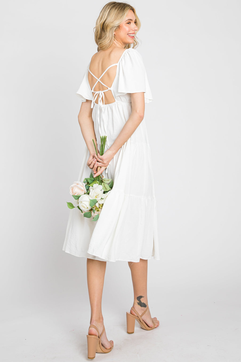 Model wearing a white tiered midi dress with short flounce sleeves and a criss cross tie back detail.