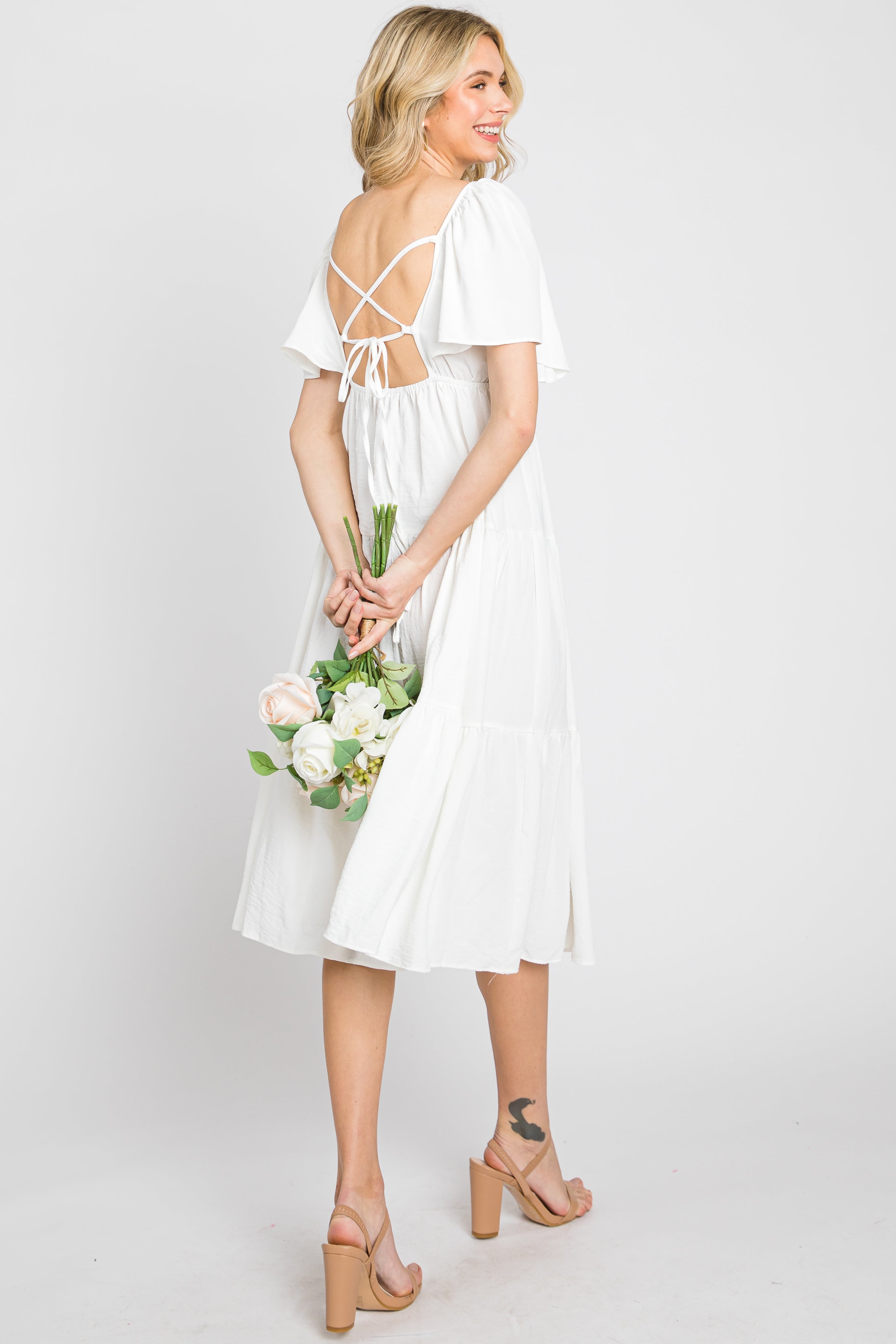 Model wearing a white tiered midi dress with short flounce sleeves and a criss cross tie back detail.
